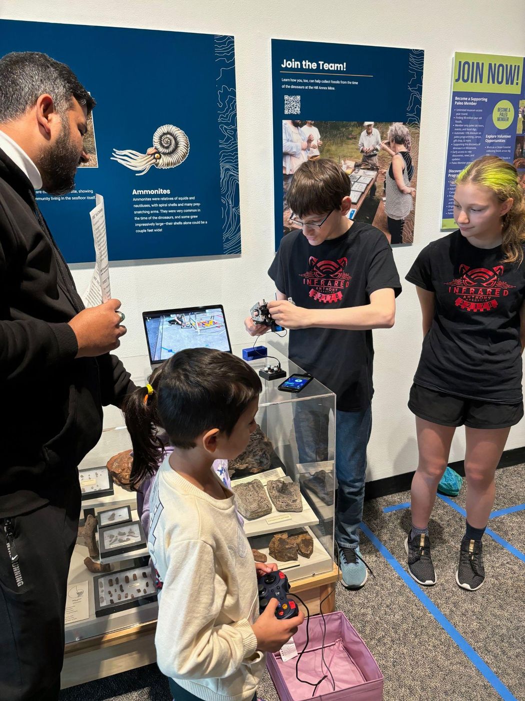 Team members showing a young visitor how to drive our robot at a museum booth